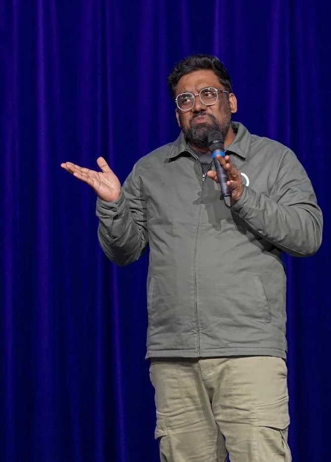 Manan Desai performing with a microphone in a grey-green jacket at The Lavari Show